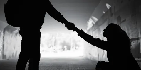 Silhouette of a person extending a hand to help someone up from a seated position.