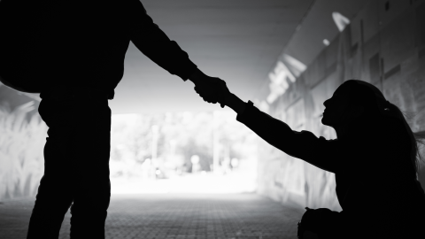 Silhouette of a person extending a hand to help someone up from a seated position.