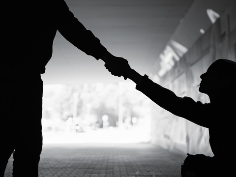 Silhouette of a person extending a hand to help someone up from a seated position.